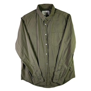 May include: An olive green long-sleeve button-down shirt featuring a standard collar, a single chest pocket on the left side, and a front button placket. The interior neck label displays the brand name FRAME in black text on a white background.