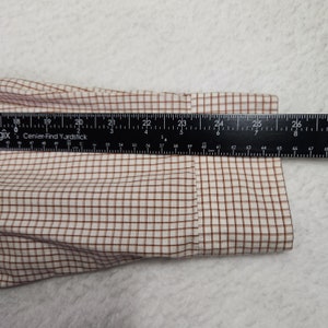 May include: Close-up of a white and brown plaid shirt cuff with a ruler measuring 26 inches.
