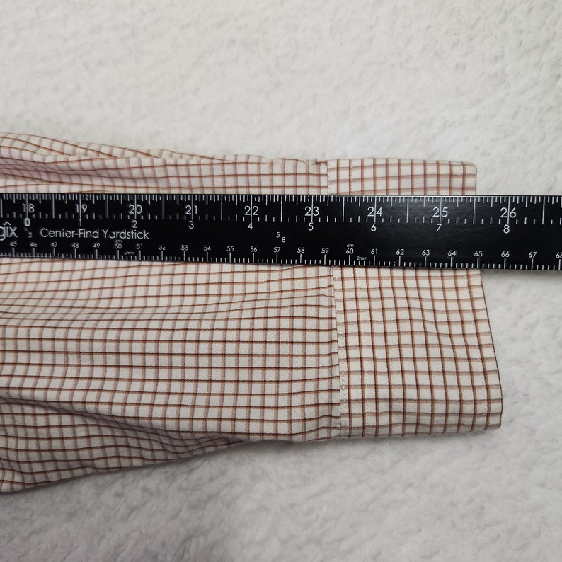 May include: Close-up of a white and brown plaid shirt cuff with a ruler measuring 26 inches.