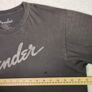 Puede incluir: Camiseta Fender gris oscuro con el logo Fender en blanco. La camiseta es 100% algod&oacute;n y tiene cuello redondo. La camiseta es talla L.
