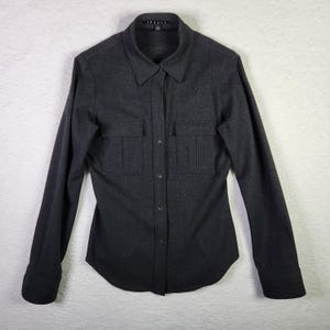May include: A dark gray long-sleeved button-down shirt with two flap pockets on the front. The shirt has a collar and a button closure.