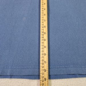 May include: A close-up of blue fabric with a ruler alongside. The ruler shows both inches and centimetres. The fabric is a solid colour and has a smooth texture. The ruler measures up to 29 inches.