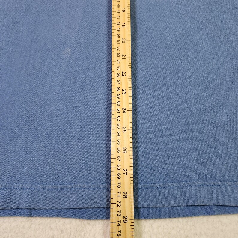 May include: A close-up of blue fabric with a ruler alongside. The ruler shows both inches and centimetres. The fabric is a solid colour and has a smooth texture. The ruler measures up to 29 inches.