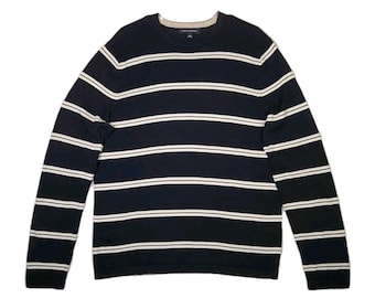 May include: A navy blue long-sleeved sweater with horizontal white stripes. The sweater has a crew neck and a neutral-colored neckline. The sleeves are long and the material appears to be a knit fabric.