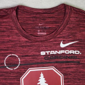 Puede incluir: Camiseta deportiva DRI-FIT granate y negra. La camiseta presenta el logo de Nike y el texto "STANFORD CARDINAL". Un gr&aacute;fico blanco de un &aacute;rbol es visible en la camiseta.