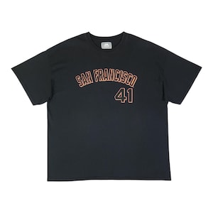 May include: A black short-sleeve t-shirt featuring the text SAN FRANCISCO in an arched orange font above the number 41 in a matching orange font. The shirt has a crew neckline and a Majestic brand label on the inside of the collar.