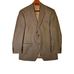 May include: A tan blazer with a two-button closure, notched lapels, and two front pockets. The blazer is hanging on a wooden hanger against a white background. The interior lining is a light brown color.