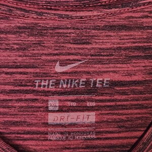 Puede incluir: Primer plano de una camiseta deportiva roja y negra con el logo de Nike y el texto "THE NIKE TEE". La camiseta tiene un patr&oacute;n texturizado y las palabras "DRI-FIT" son visibles.