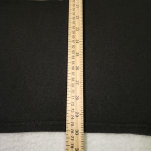 Puede incluir: Primer plano de una tela negra con una regla amarilla que mide de 53 a 78 cm. La regla tiene marcas para cada cent&iacute;metro e incrementos m&aacute;s peque&ntilde;os. La tela parece ser de un color s&oacute;lido.