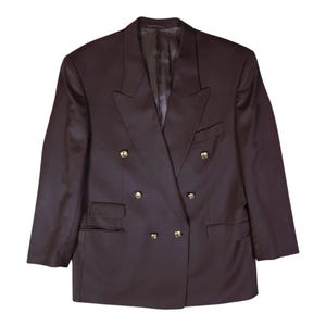 Op de afbeelding: Een donkerbruine double-breasted blazer met een gestructureerde kraag, lange mouwen en zes goudkleurige knopen in twee verticale rijen. Het kledingstuk heeft twee zijzakken met klep en een borstzak aan de linkerzijde.