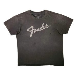 Puede incluir: Camiseta gris oscuro con el logotipo de Fender en escritura blanca en la parte delantera. La camiseta tiene cuello redondo y mangas cortas. El logotipo de Fender tambi&eacute;n est&aacute; impreso en la etiqueta.