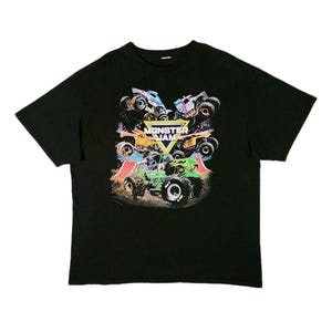 Puede incluir: Camiseta negra con un gr&aacute;fico colorido de monster trucks. El dise&ntilde;o incluye las palabras "Monster Jam" en amarillo y blanco, con varios monster trucks de diferentes colores. La camiseta est&aacute; hecha de un material suave.