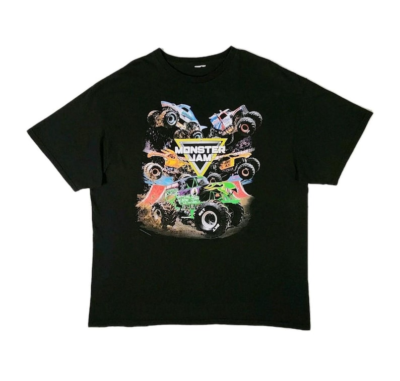 Puede incluir: Camiseta negra con un gr&aacute;fico colorido de monster trucks. El dise&ntilde;o incluye las palabras "Monster Jam" en amarillo y blanco, con varios monster trucks de diferentes colores. La camiseta est&aacute; hecha de un material suave.