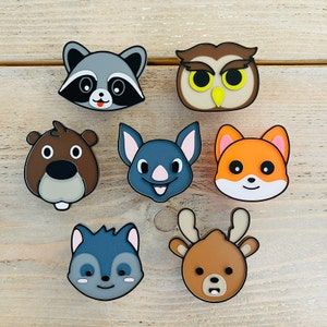 May include: Set of eight colourful animal-shaped pins. The pins feature a raccoon, owl, beaver, bat, fox, deer, and two different types of squirrels. The pins are made of a hard plastic material and have a shiny finish.
