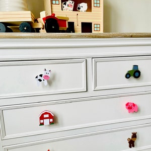 May include: White chest of drawers with six drawers featuring farm animal themed drawer pulls. The pulls include a cow, a tractor, a pig, a barn, a chicken, and a horse.