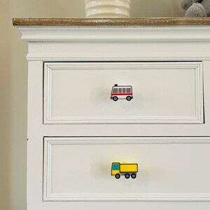 May include: White dresser with two drawers. The top drawer has a red and white bus-shaped knob. The bottom drawer has a yellow truck-shaped knob.