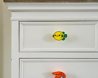 May include: White dresser with two drawers. The top drawer has a yellow and green pufferfish drawer pull. The bottom drawer has an orange and red shrimp drawer pull.