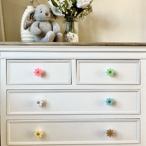 May include: White chest of drawers with four drawers and flower-shaped knobs in pink, green, blue, white, and yellow.