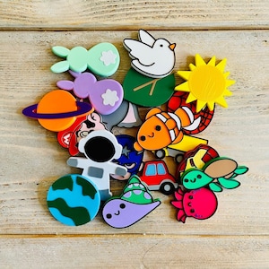 May include: A collection of colourful, whimsical, and playful character-shaped silicone bath toys. The toys include a fish, a turtle, a sun, a spaceship, a dinosaur, a butterfly, a flower, and a few other characters.