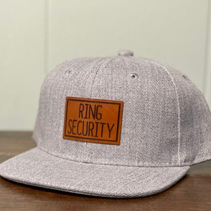 May include: Gray and brown baseball cap with a leather patch that says "Ring Security".