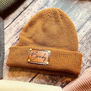 May include: A brown knit beanie with a leather patch that says "Brady" on it.
