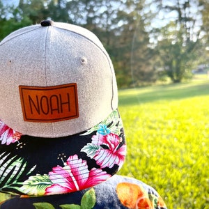 May include: A gray and black baseball cap with a brown leather patch that says "NOAH" on it. The cap has a floral print on the underside of the brim.