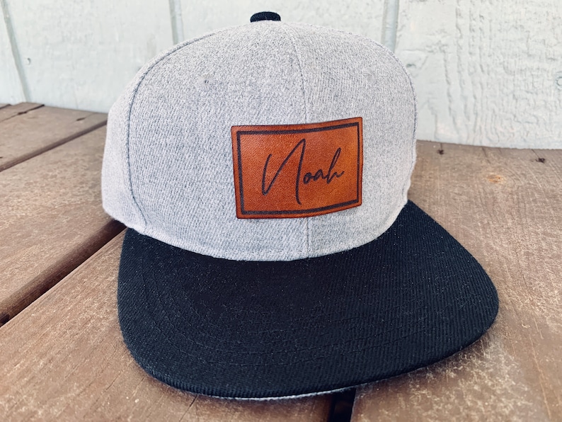May include: A gray and black baseball cap with a brown leather patch that says "Noah" in cursive.