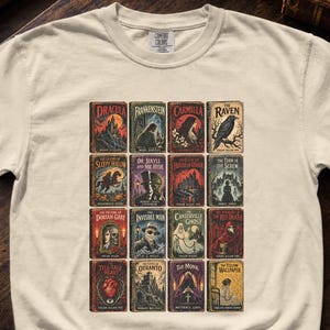 Pode incluir: Uma t-shirt de manga curta cor de creme com uma impressão gráfica de dezasseis capas de livros de literatura gótica clássica dispostas numa grelha. Os títulos incluem Dracula, Frankenstein, Carmilla, The Raven, Sleepy Hollow e outros.