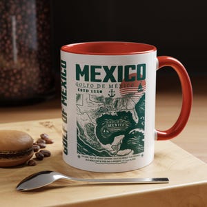 Könnte beinhalten: Weiße Keramik-Kaffeetasse mit rotem Rand. Die Tasse zeigt eine grüne Vintage-Karte des Golfs von Mexiko mit dem Text "Mexico, Golfo de Mexico, Est. 1550".