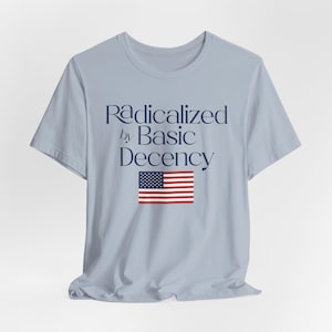 Può includere: Maglietta blu chiaro con il testo "Radicalized by Basic Decency" e una grafica della bandiera americana.