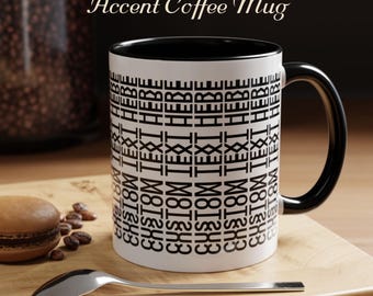 May include: A white accent coffee mug with a black interior and handle. The mug features the text "HERE CUSTOM TEXT" in a repeating pattern. A spoon and a macaron are on a wooden surface.
