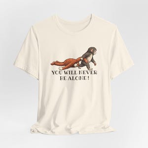 May include: Cream-colored t-shirt featuring a graphic of a brown monkey pulling a brown teddy bear. A dark gray monkey is walking. The text "YOU WILL NEVER BE ALONE!" is printed below the graphic.