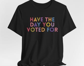 Op de afbeelding: Zwart T-shirt met de tekst "HAVE THE DAY YOU VOTED FOR" in regenboogkleuren.