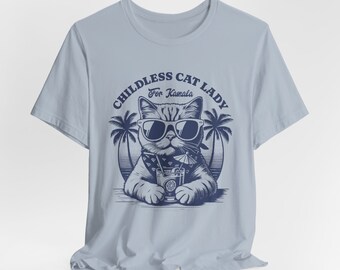 May include: Light blue t-shirt with a graphic of a cat wearing sunglasses and a bandana, holding a cocktail. The text "Childless Cat Lady For Kamala" is printed in a circle around the cat.