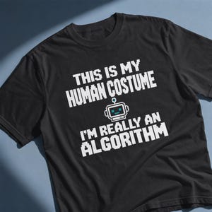 May include: A black short-sleeved t-shirt featuring white pixelated text that reads THIS IS MY HUMAN COSTUME I'M REALLY AN ALGORITHM. Centered between the two lines of text is a small white and light blue pixelated graphic of a robot head.