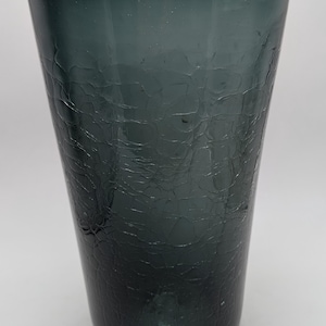 May include: A tall, tapered glass vase in a deep charcoal gray color. The exterior surface features a distinct crackle texture, creating a network of fine, irregular lines across the translucent glass body, which widens toward the top rim.