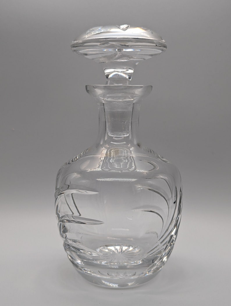 May include: A clear glass decanter with a stopper. The decanter has a round body with a textured design and a tall, slender neck. The stopper is also clear glass and has a round, flat top.