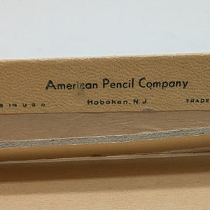 May include: Close-up of a beige box with black text that reads "American Pencil Company, Hoboken, N.J., Trade Mark Reg., Made in U.S.A."