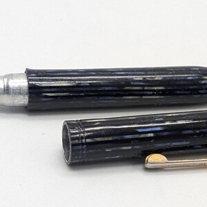 May include: A black and silver pen with a striped pattern and a gold-colored clip. The pen is disassembled, showing the inner workings.