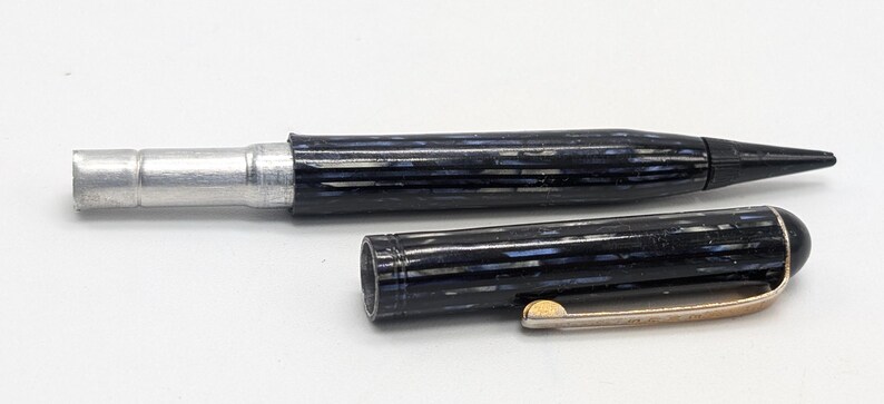 May include: A black and silver pen with a striped pattern and a gold-colored clip. The pen is disassembled, showing the inner workings.