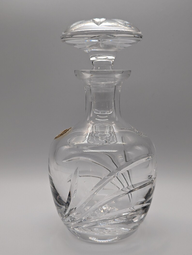 May include: A clear glass decanter with a cut glass design. The decanter has a stopper with a cut glass design.