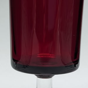 May include: A clear glass stemmed goblet with a deep red, almost burgundy, colored body. The goblet has a wide base and a round bowl.