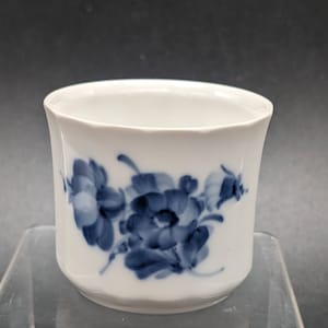 May include: A white porcelain cup with a blue floral design. The cup has a rounded shape and a slightly flared rim.