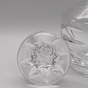 May include: A clear glass bottle stopper with a starburst design and a flower-shaped rim.