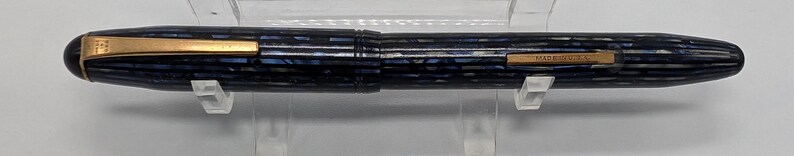 May include: A blue and gold fountain pen with a striped pattern and the words "MADE IN USA" on the side.