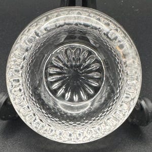 May include: A clear glass candle holder with a decorative, starburst-shaped design on the bottom.