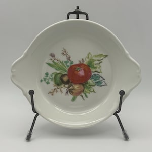 May include: White ceramic baking dish with a floral design featuring a red tomato, green leaves, and other vegetables. The dish has two handles on the sides.