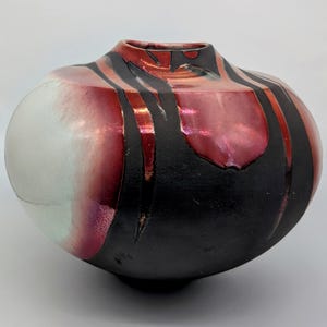 May include: A round ceramic vase with a black and red glaze. The vase has a wide mouth and a rounded bottom. The glaze is uneven, creating a mottled effect.