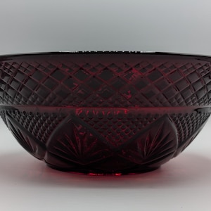 May include: A deep red glass bowl with a diamond and fan pattern. The bowl has a wide, open shape and is likely used for serving or display. The glass has a glossy finish, reflecting light and adding to its visual appeal.