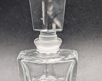 May include: A clear glass bottle with a square base and a rectangular stopper. The bottle is empty and has a frosted finish.